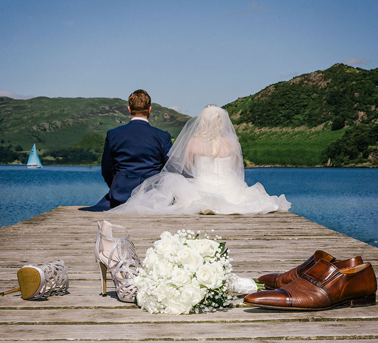 Bride and Groom Sitting at the End of a Jetty Overlooking a Large Lake