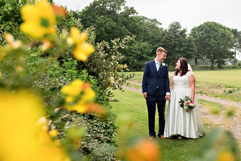 Bride and Groom Holding Hands near Yellow Shrubs