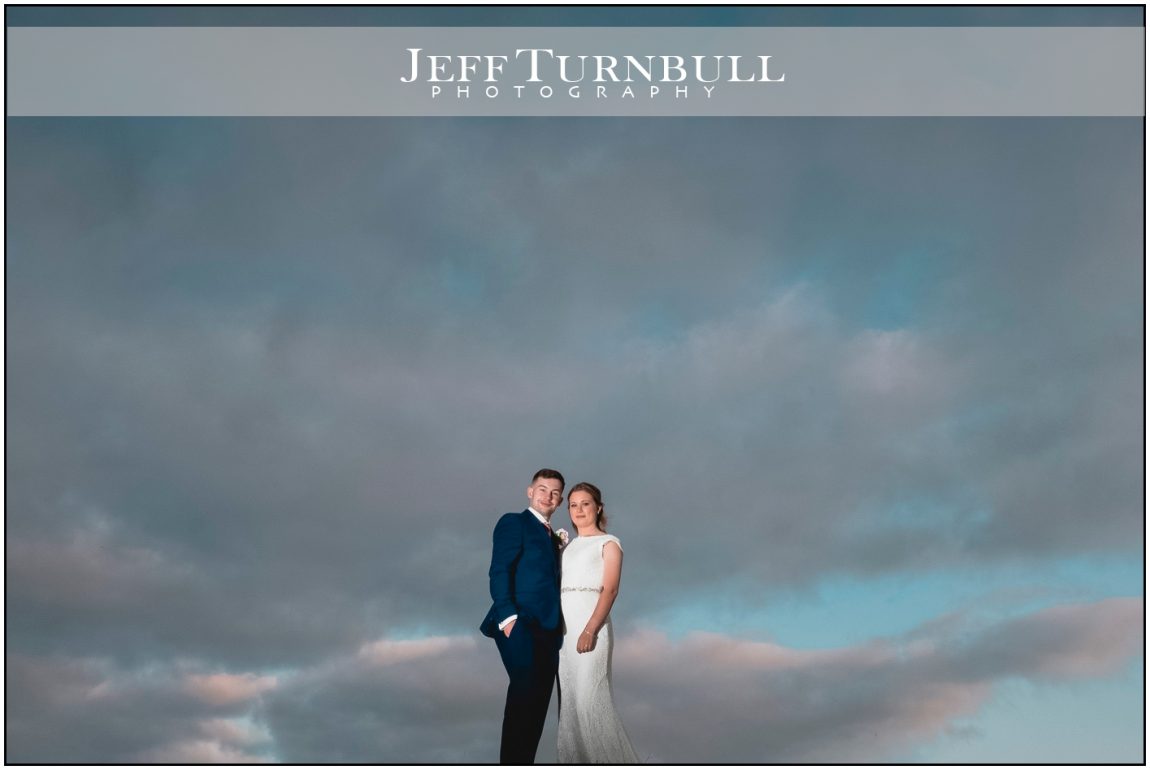 Bride and Groom Standing Together with a Dramatic Sky Behind Them